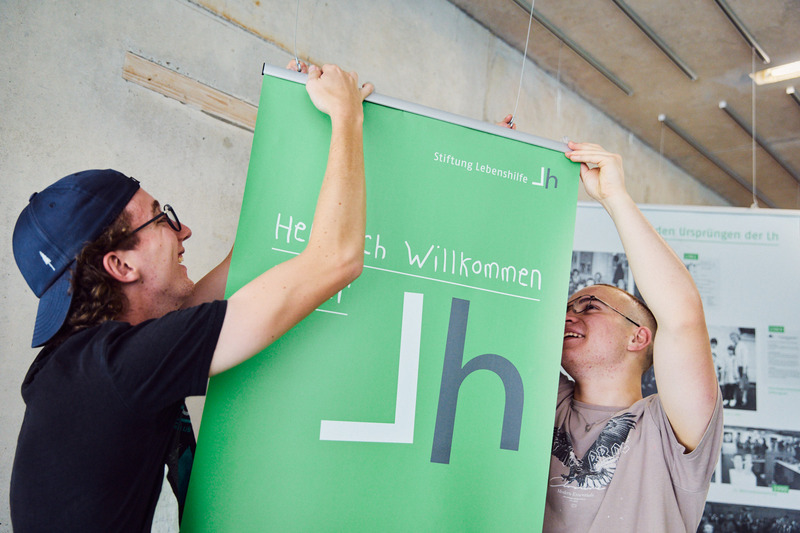 Zwei Mitarbeiter hängen ein Schild auf.