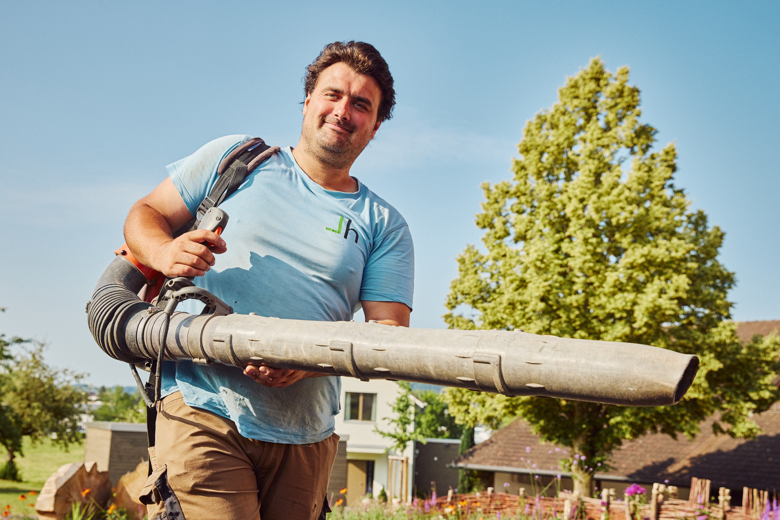 Geschützter Arbeitsplatz im Gartenbau: Ein Mitarbeitender ist mit einem Laubbläser im Garten unterwegs.