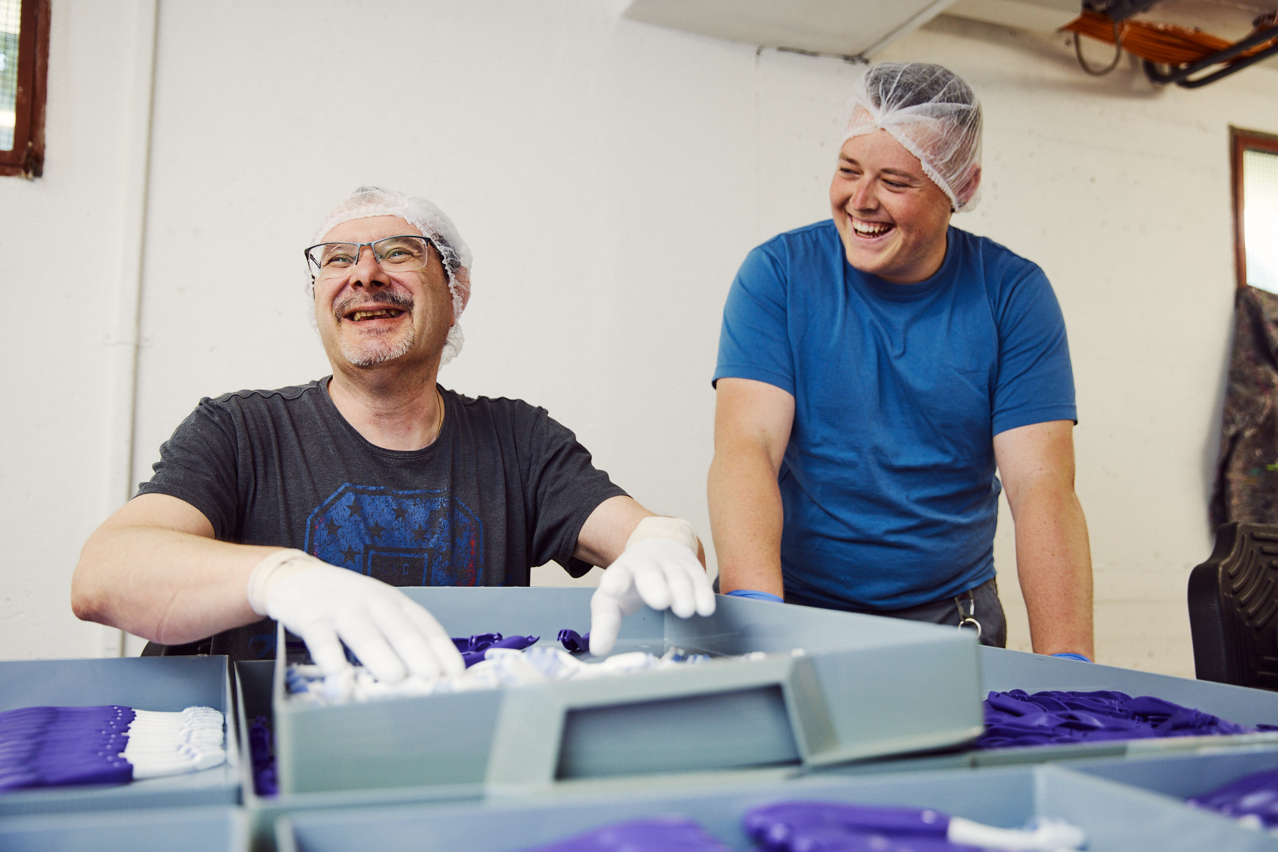 Zivildienstleistender und begleitete Person in der Werkstatt am Verpacken von Zahnbuersten.
